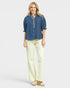Woman wearing a blue denim shirt and light yellow pants on a white background