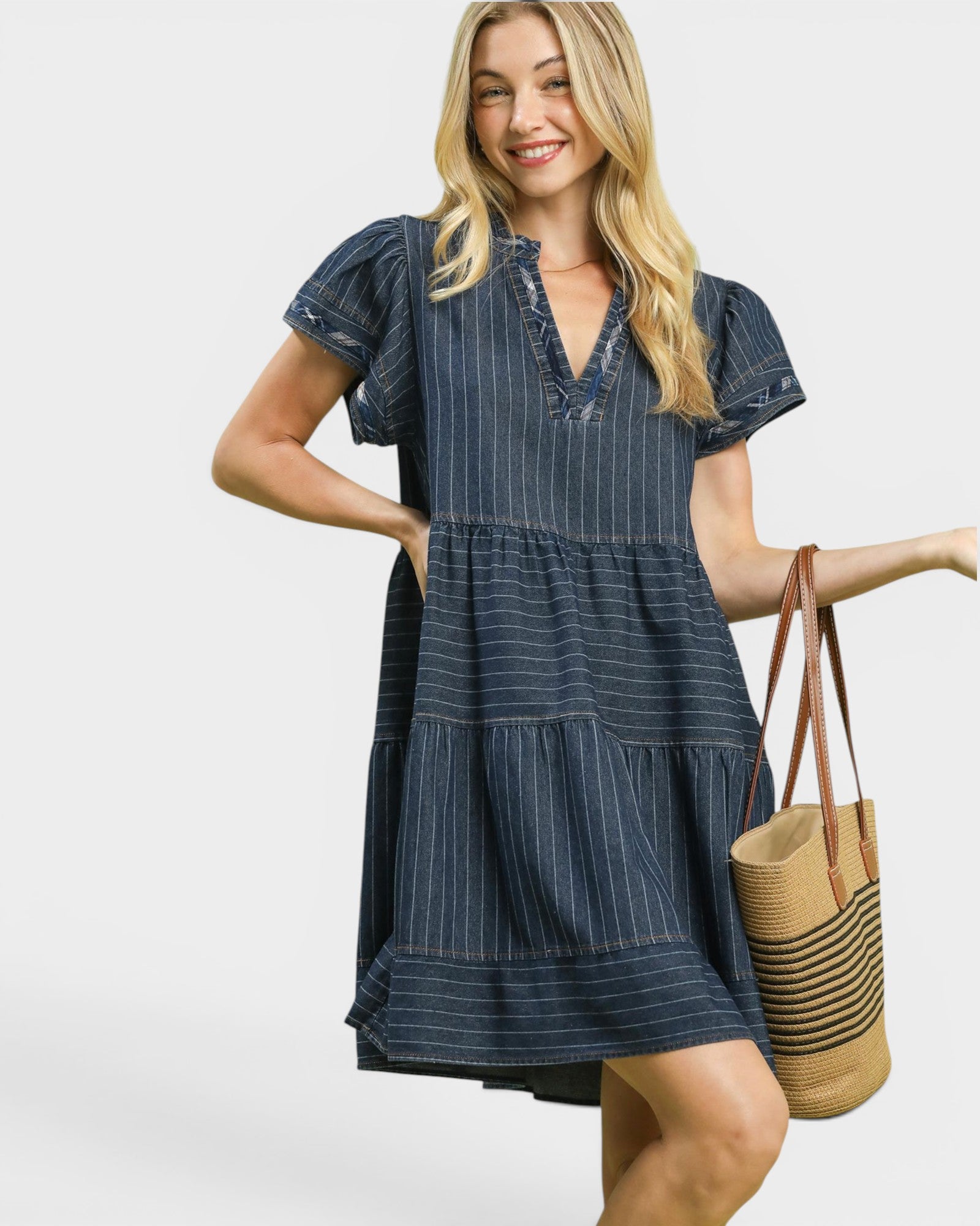 Woman wearing a blue striped dress holding a woven bag on a white background