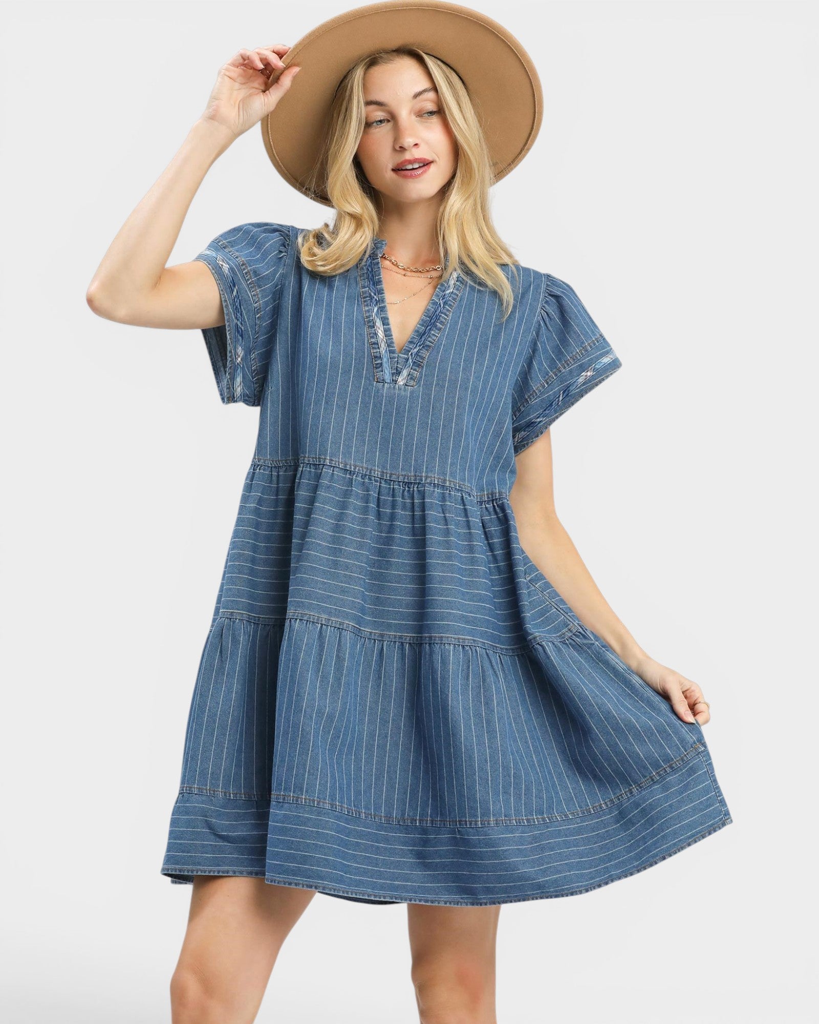 Woman wearing a blue denim dress and beige hat on a white background