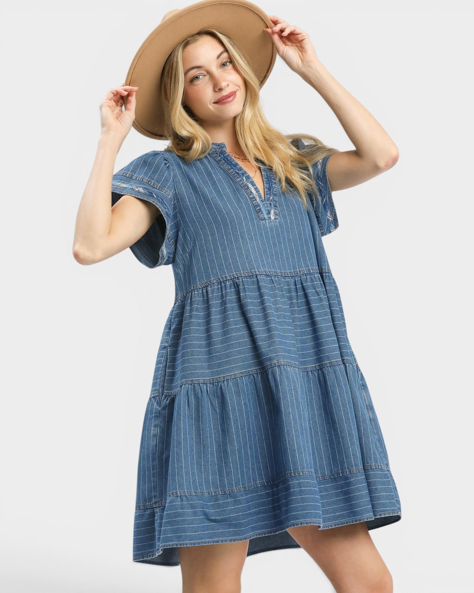 Woman wearing a blue denim dress and beige hat on a white background