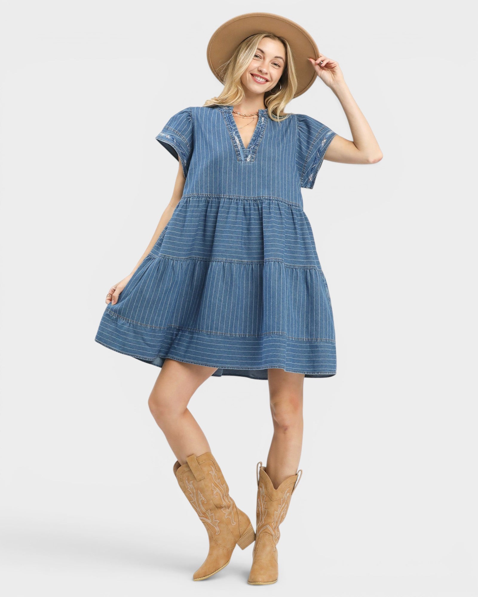 Woman wearing a blue dress with short sleeves, a hat, and brown boots on a white background
