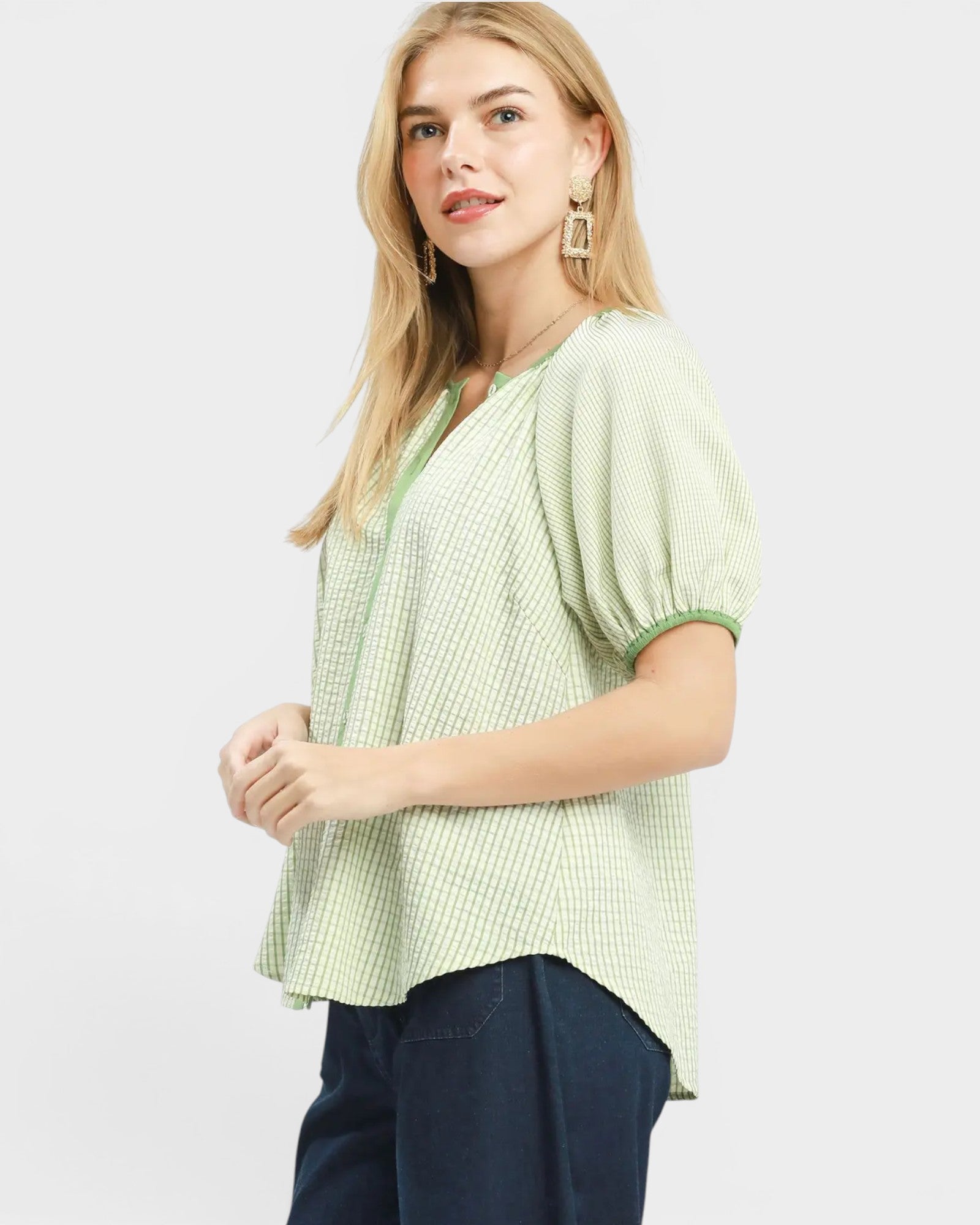 Woman wearing a light green checkered top with navy pants on a white background