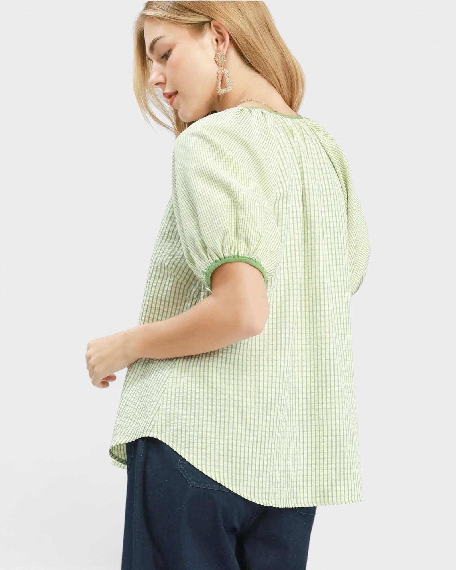 Woman wearing a light green checkered blouse with navy pants on a white background