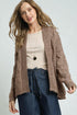 Woman wearing a brown knitted cardigan over a beige top and blue jeans on a white background