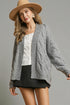 Woman wearing a gray cable knit cardigan, white top, black skirt, and beige hat on a gray background