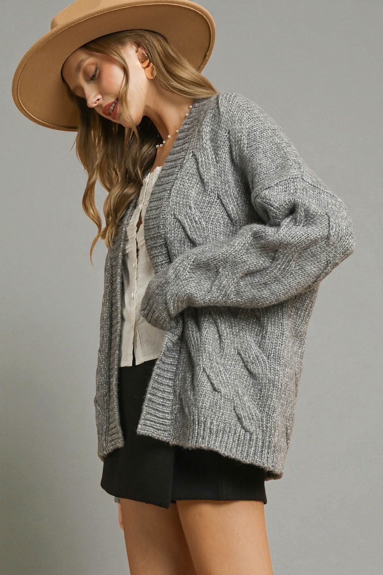 Woman wearing a gray knitted cardigan and beige hat on a plain background
