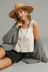 Woman wearing a beige hat, gray cardigan, and white top on a gray background