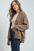 Woman wearing a brown knitted cardigan over a white shirt and blue jeans on a light gray background