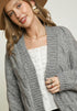 Woman wearing a gray cardigan over a white top with a plain background