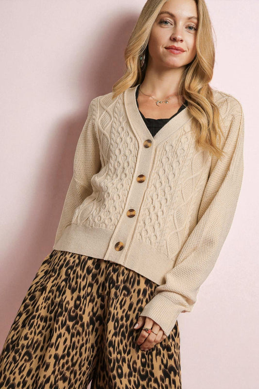 Woman wearing a beige cable knit cardigan with brown buttons and leopard print pants against a pink background