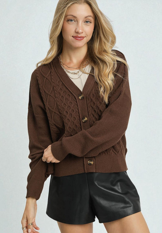 Woman wearing a brown cable knit cardigan with a plain background