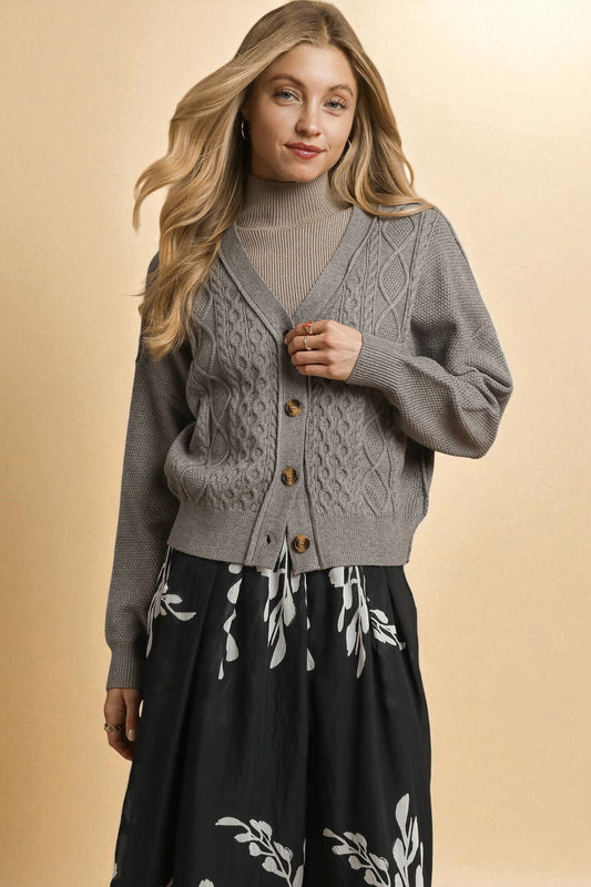 Woman wearing a gray cable knit cardigan with button details on a beige background