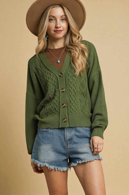 Woman wearing a green cardigan, denim shorts, and a brown hat on a beige background