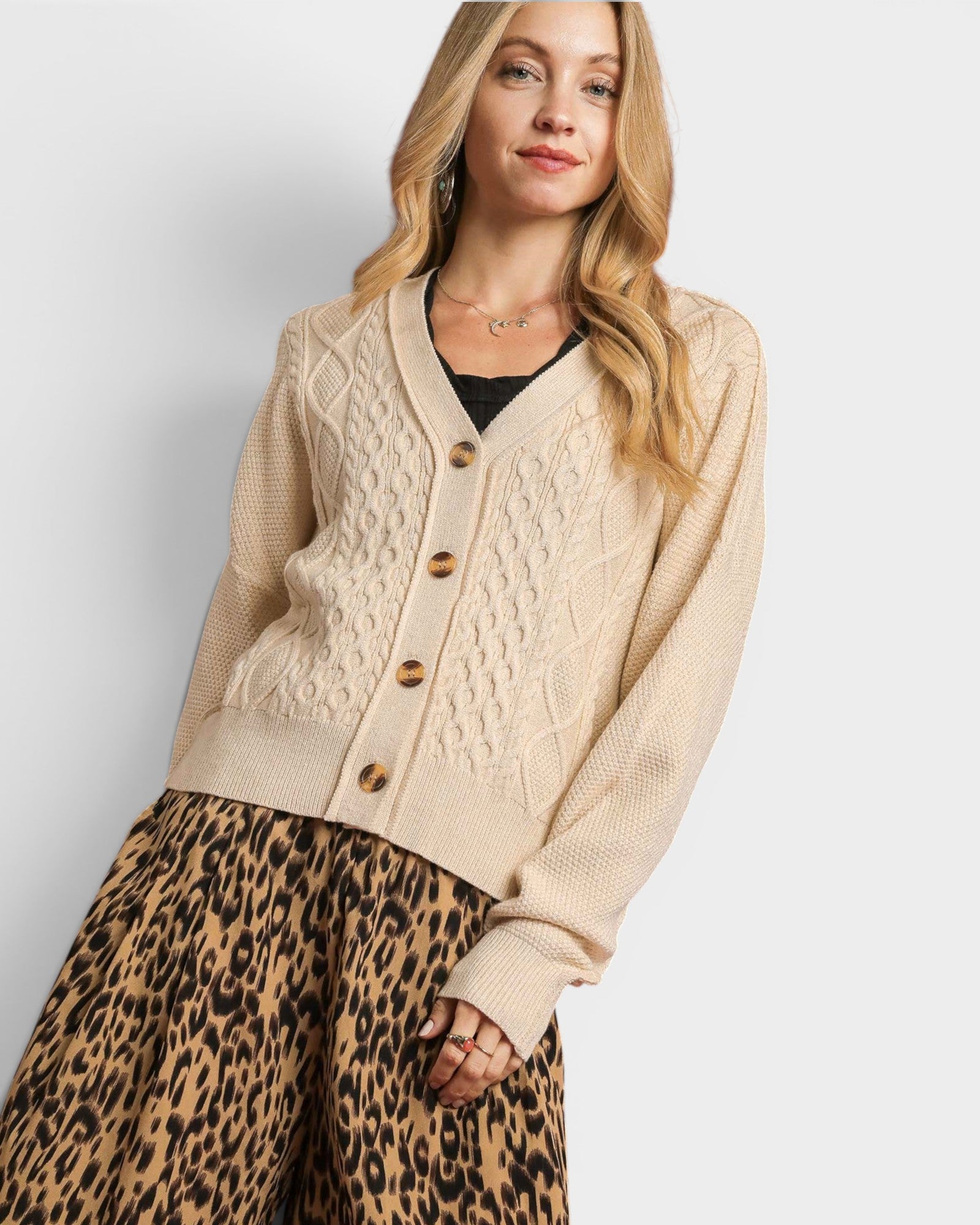 Woman wearing a beige cardigan and leopard print pants on a white background