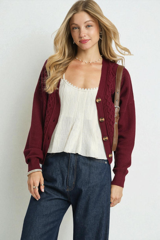 Woman wearing a burgundy cardigan, white top, and blue jeans against a plain background