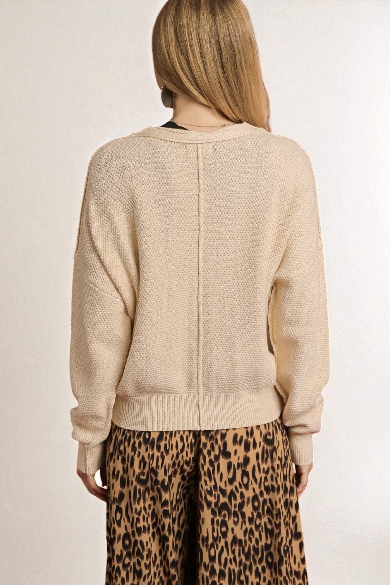 Person wearing a beige textured sweater and leopard print pants on a plain background