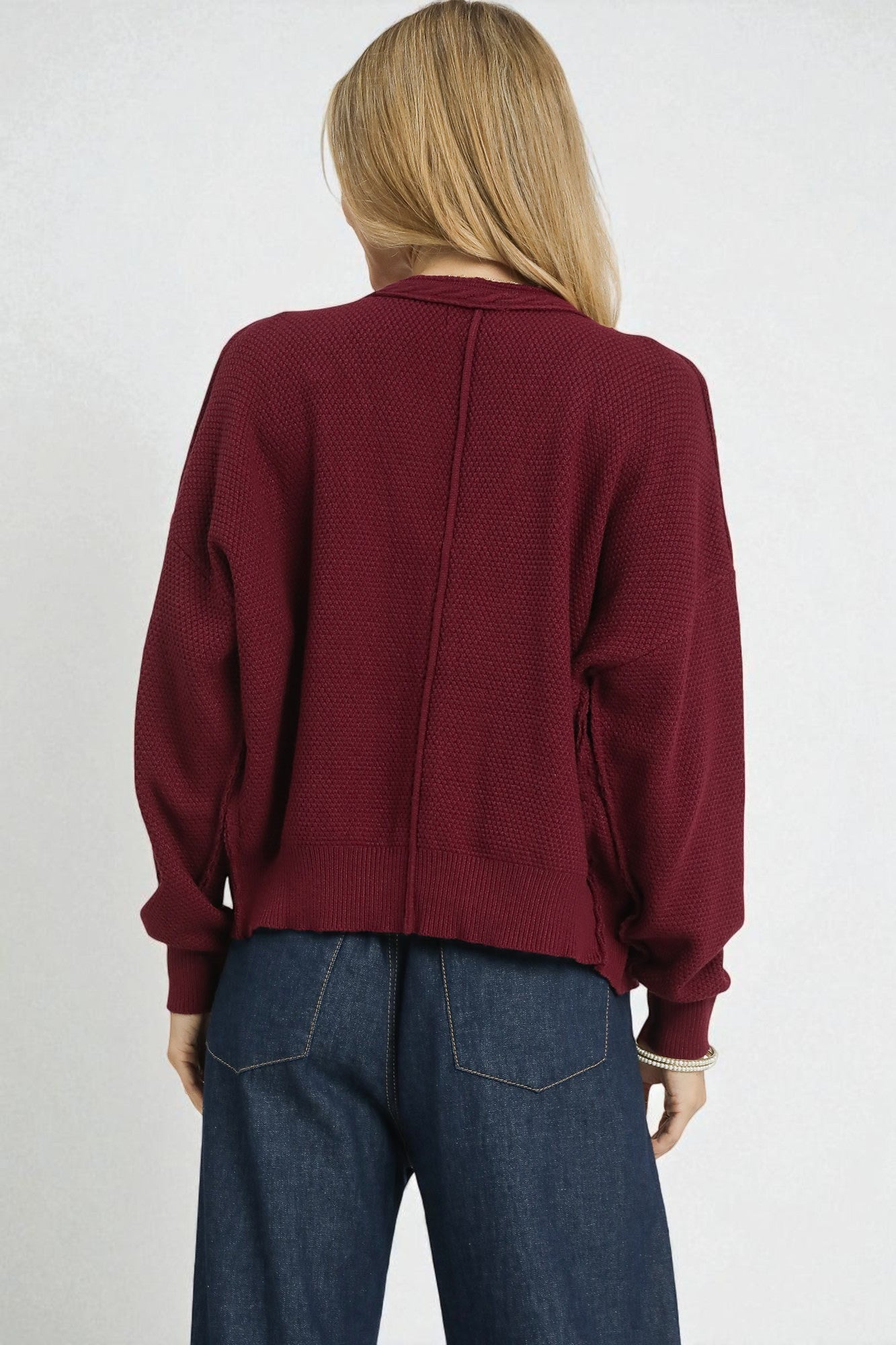 Person wearing a burgundy cardigan and blue jeans on a white background