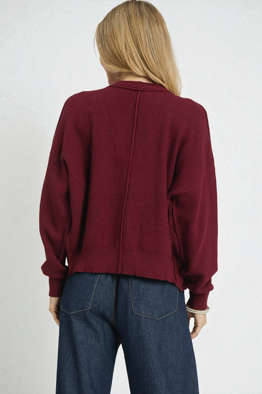 Person wearing a burgundy cardigan and blue jeans on a white background