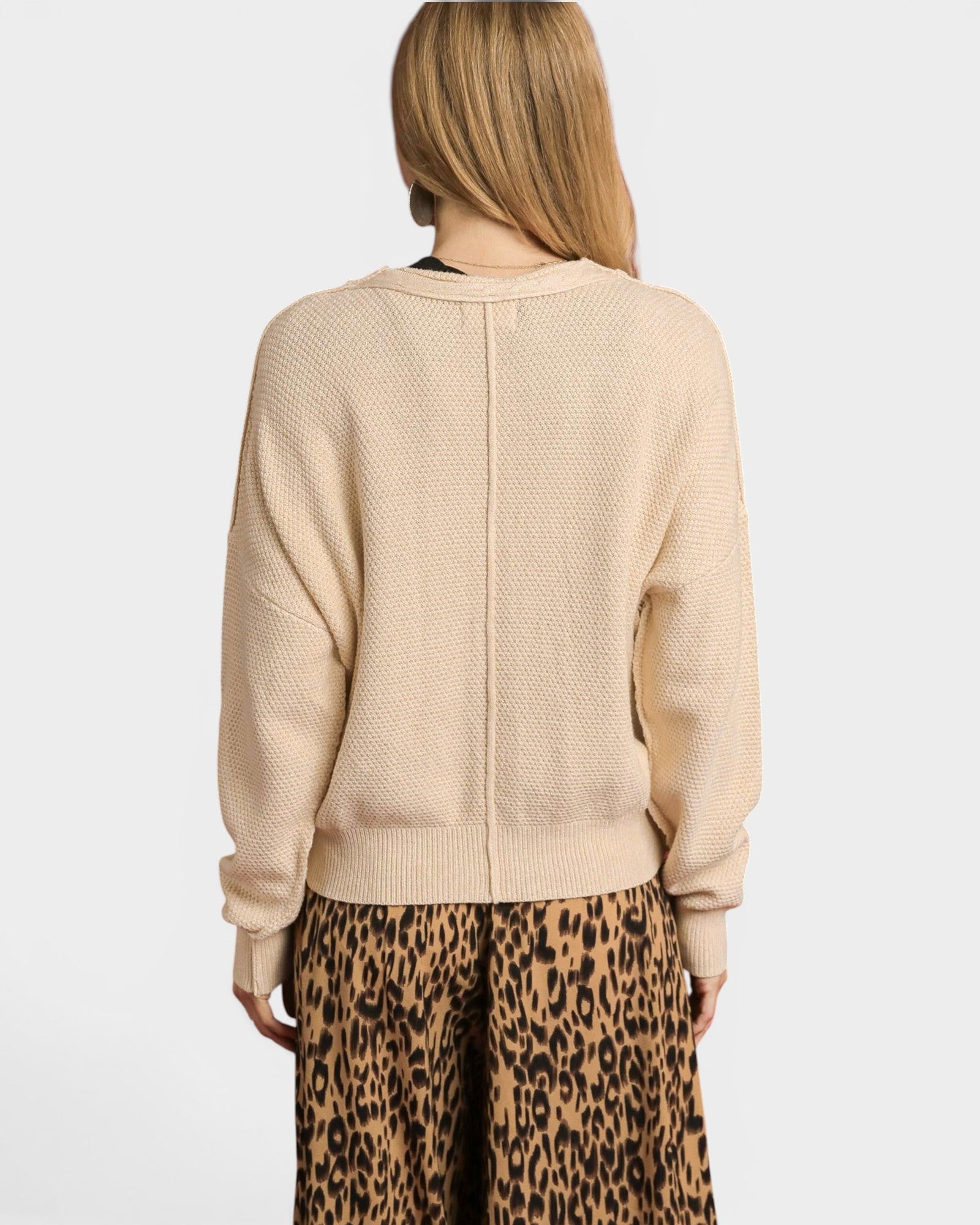 Person wearing a beige sweater and leopard print pants on a white background