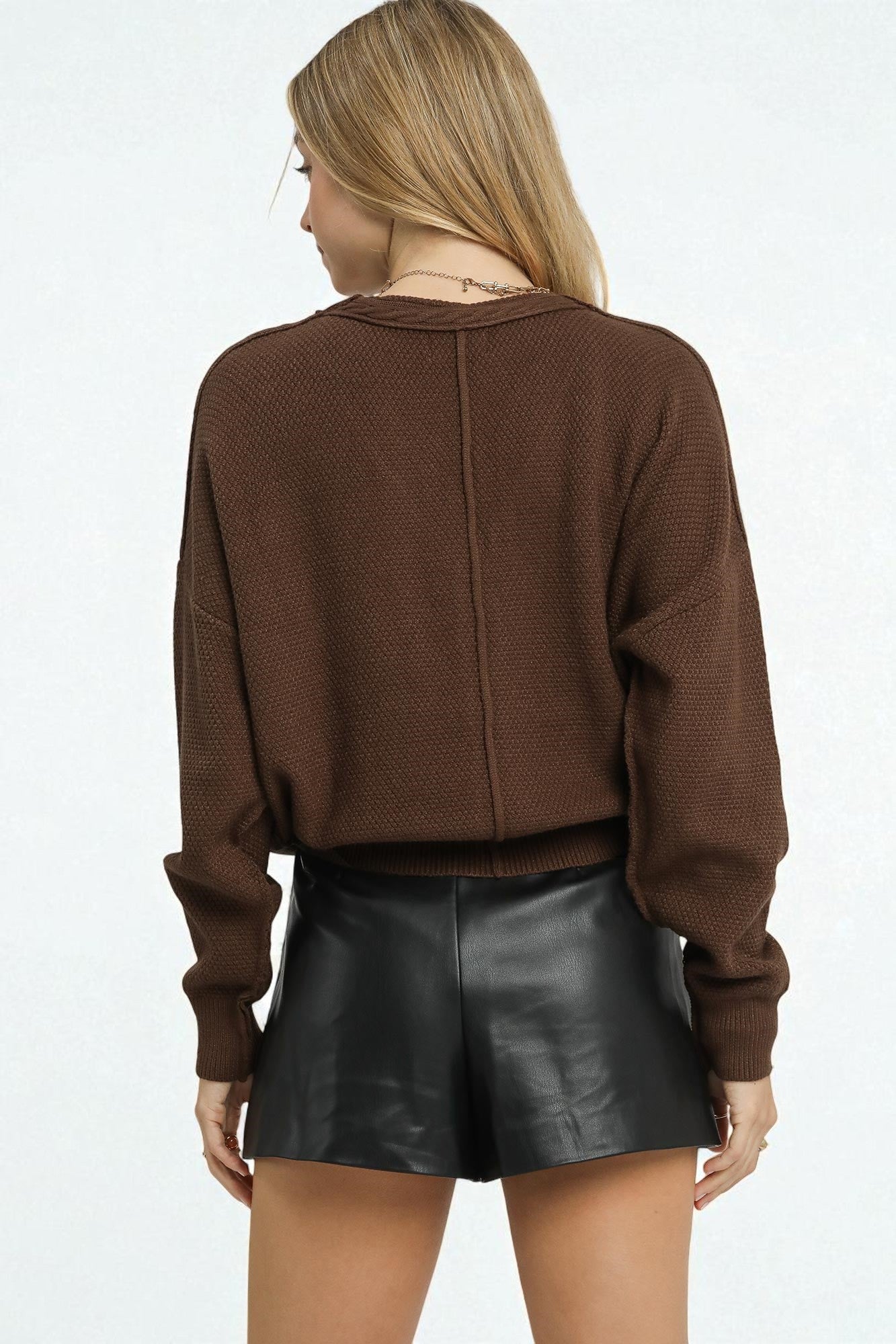Person wearing a brown sweater and black leather shorts on a white background