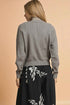 Woman wearing a gray textured cardigan over a black dress with white floral patterns on a beige background