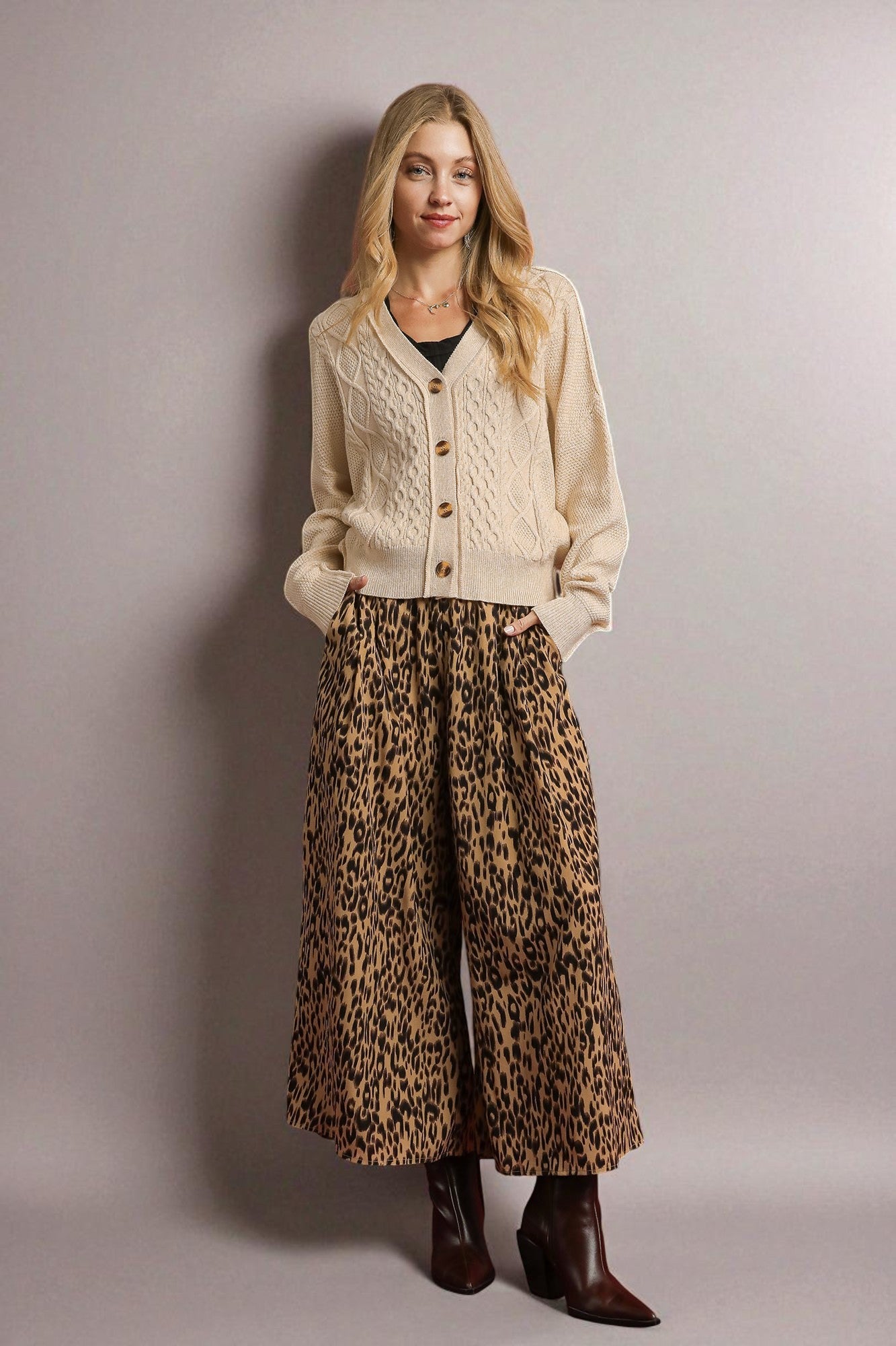 Woman wearing a beige cardigan and leopard print pants against a plain background