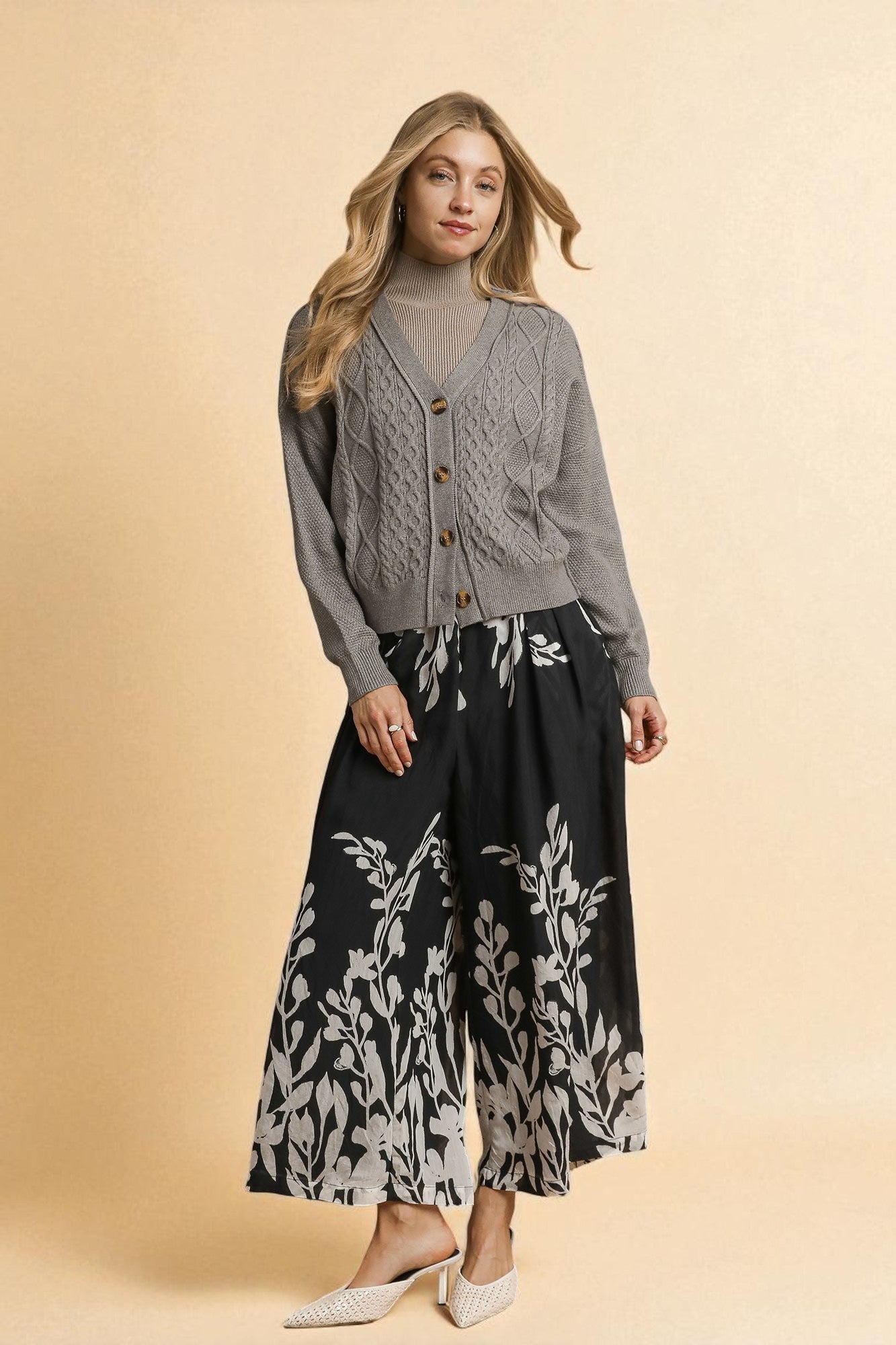 Woman wearing a gray cardigan and black floral pants on a beige background