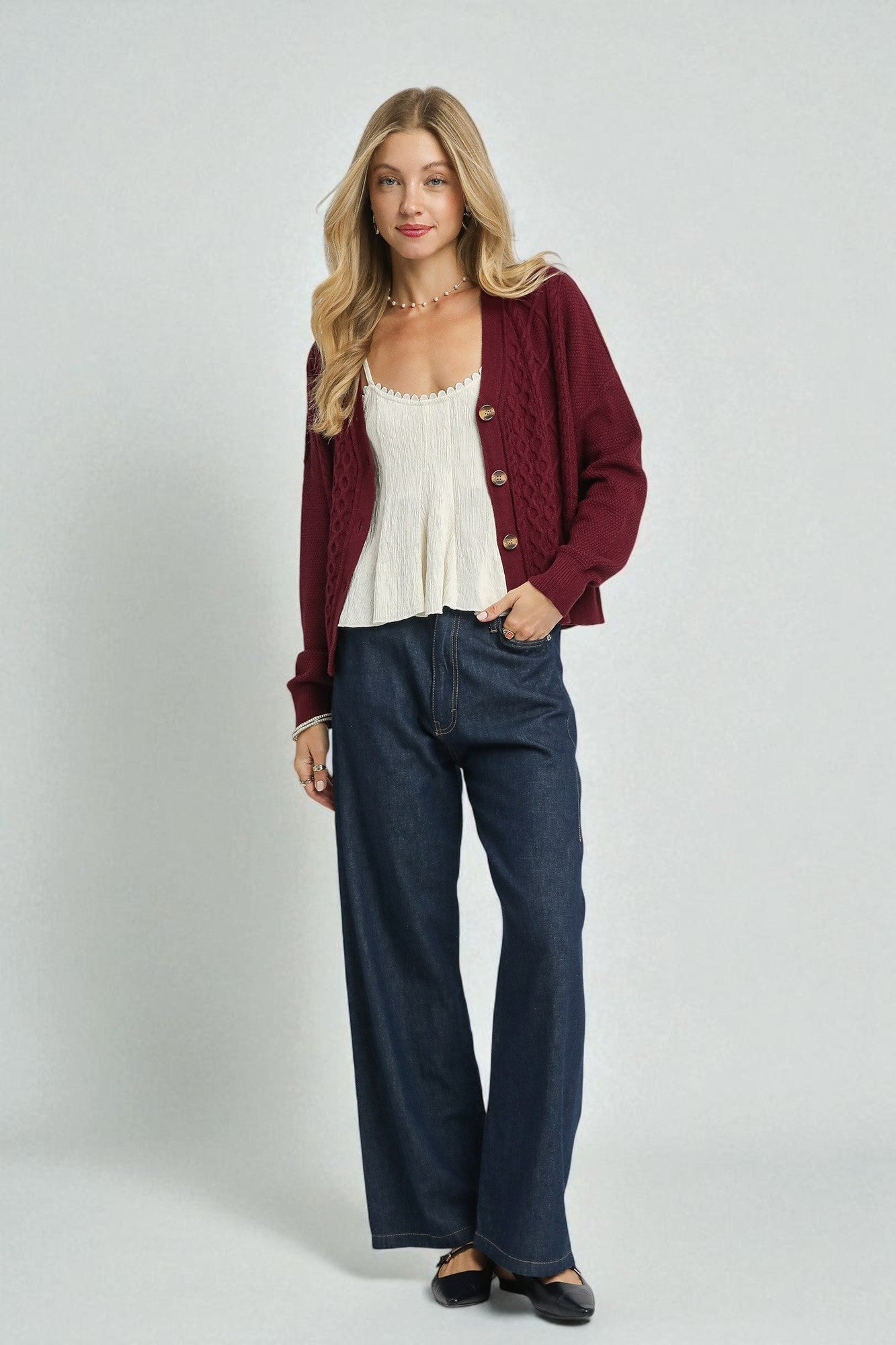 Woman wearing a red cardigan, white top, and blue jeans on a plain background