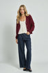 Woman wearing a red cardigan, white top, and blue jeans on a plain background