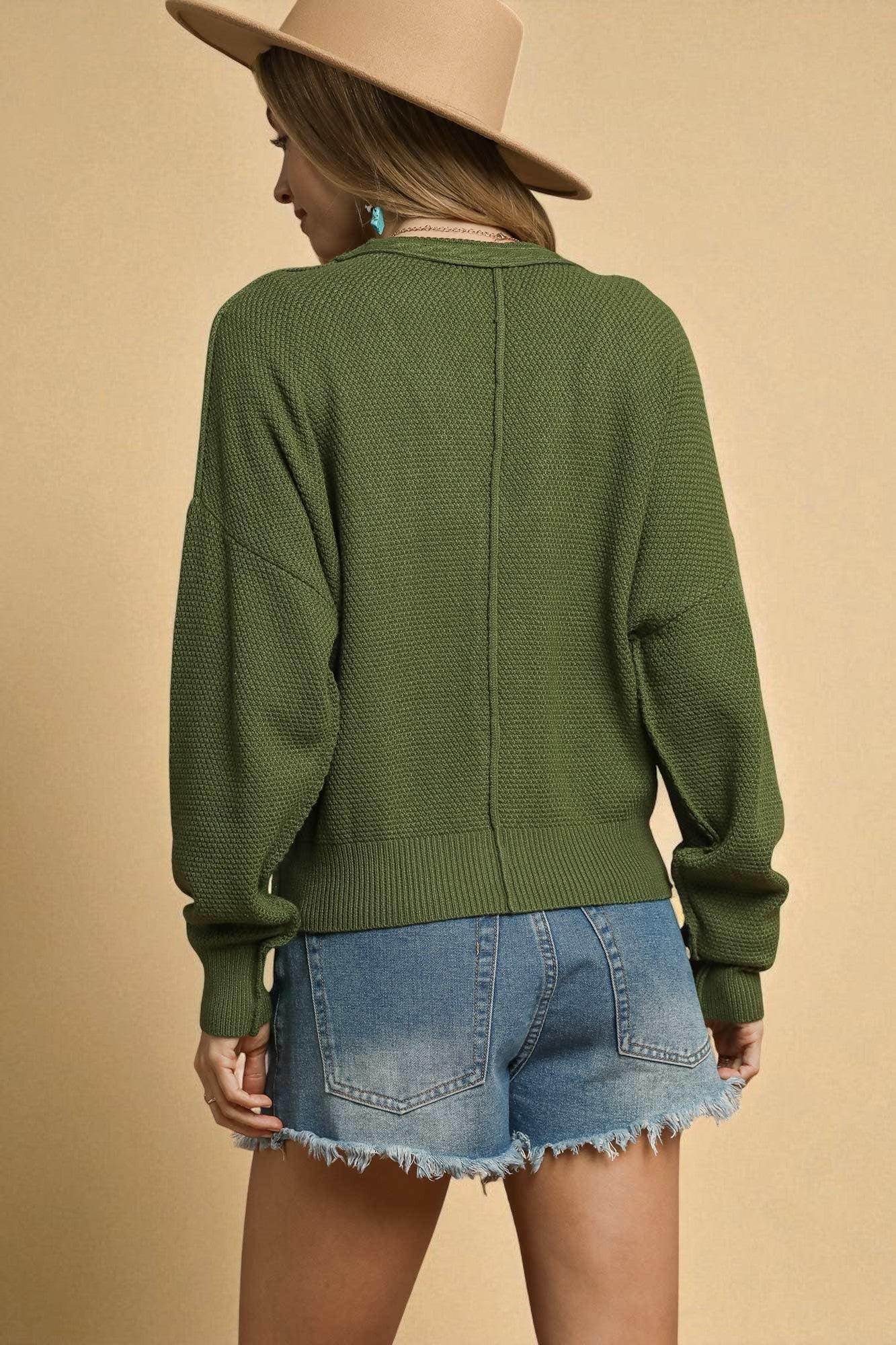 Person wearing a green sweater and denim shorts with a beige background