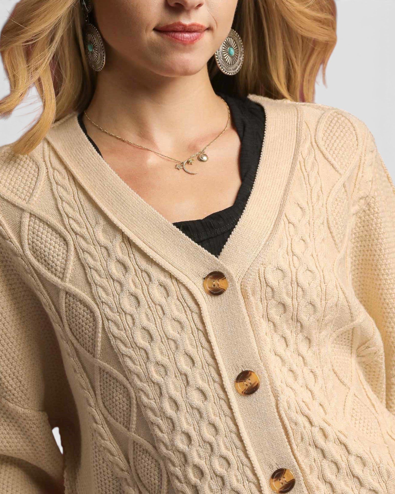 Close-up of a person wearing a beige cable knit cardigan with gold buttons.