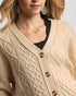 Close-up of a person wearing a beige cable knit cardigan with gold buttons.