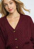 Woman wearing a burgundy cable knit cardigan with gold buttons on a white background