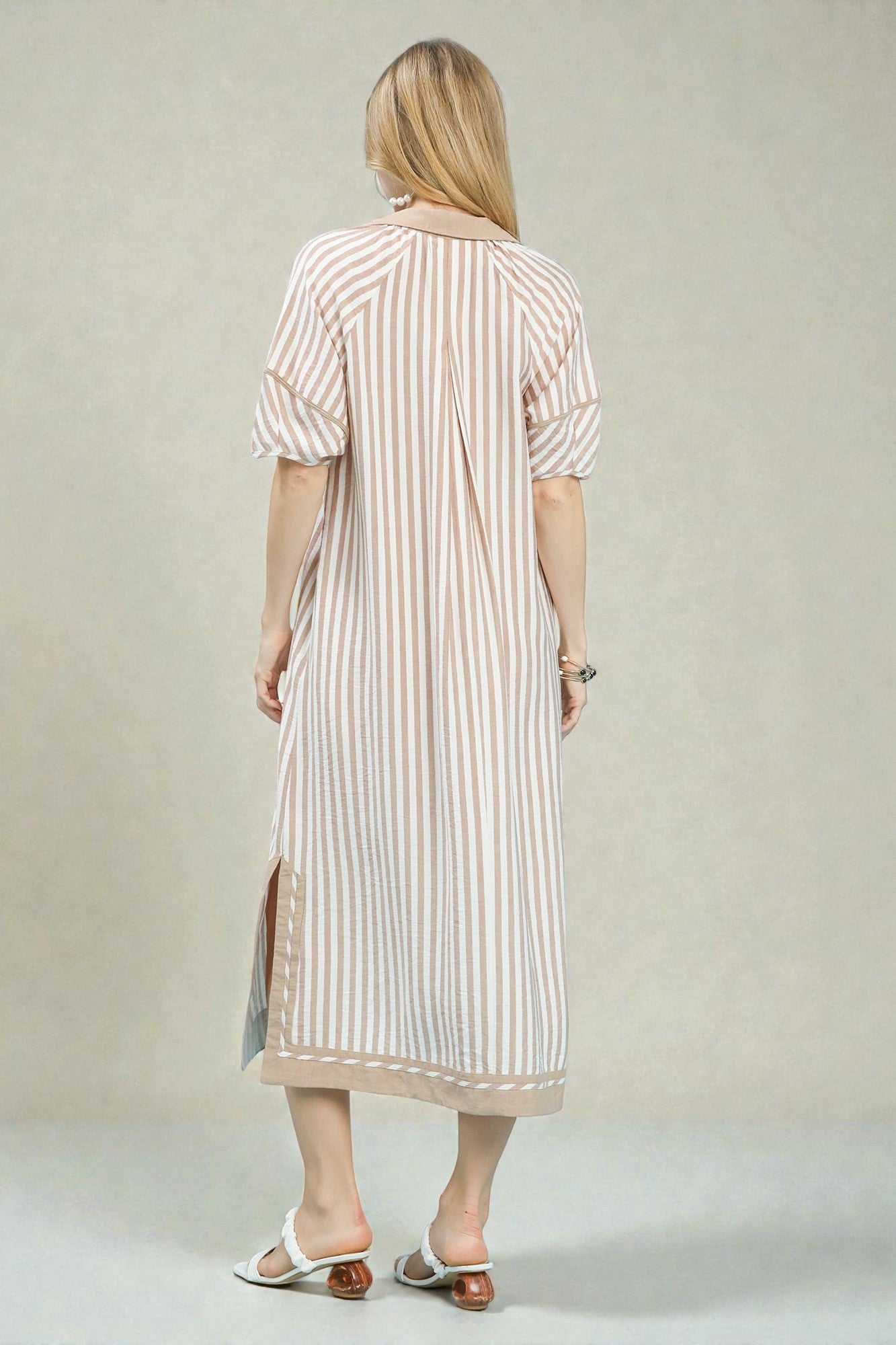 Woman wearing a long, light-colored striped dress against a plain background