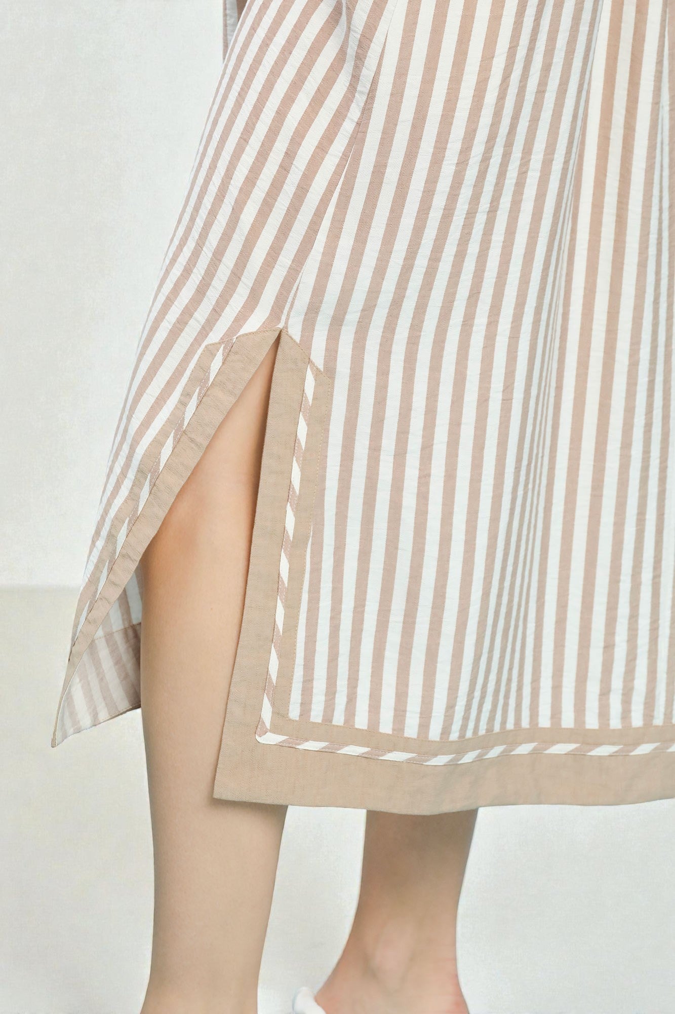 Close-up of a person wearing a beige and white striped dress with a slit on a light background