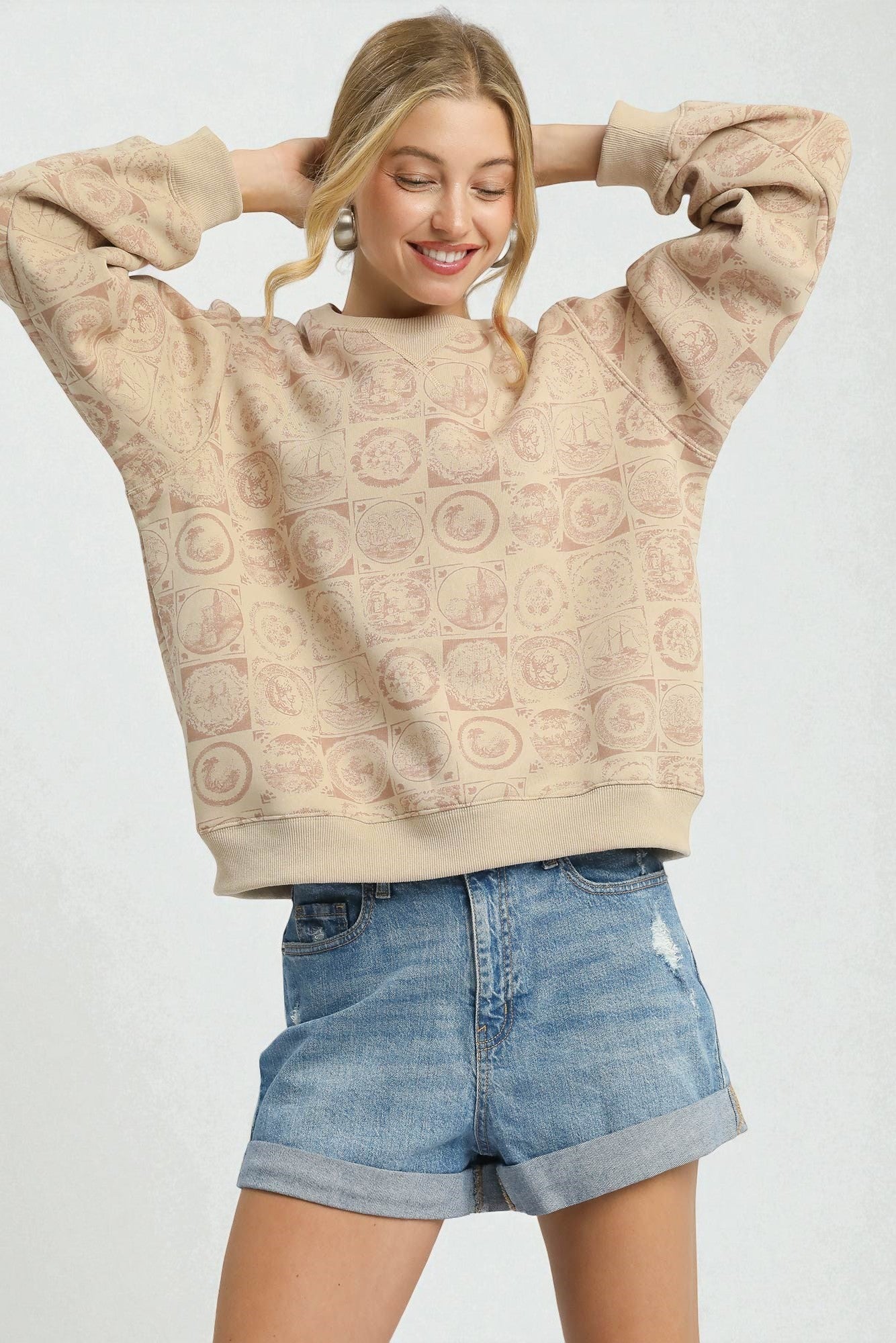 Woman wearing a beige patterned sweatshirt and denim shorts on a white background