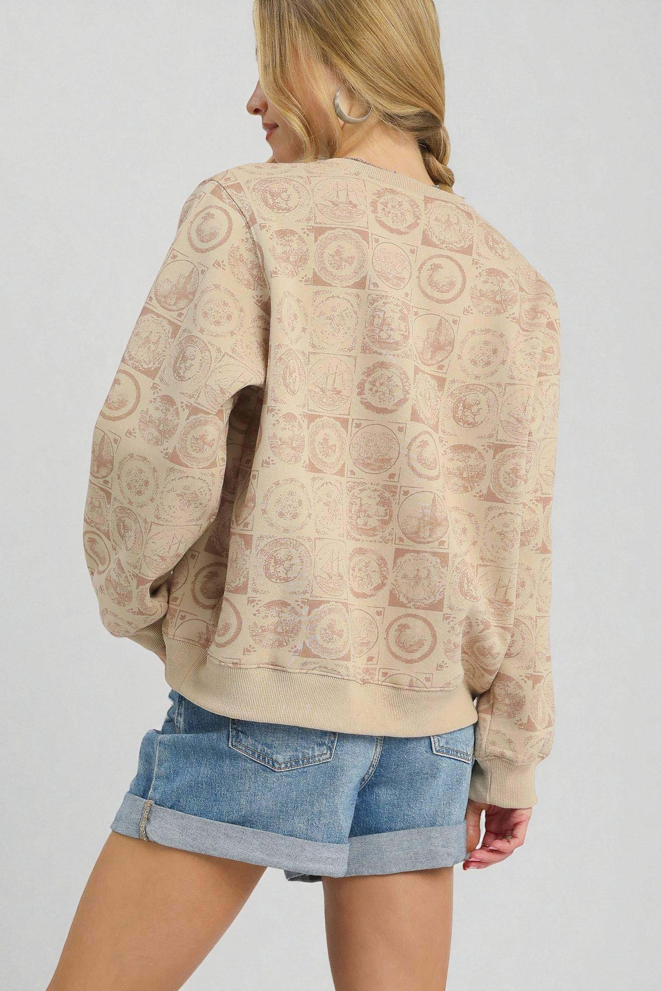 Woman wearing a beige patterned sweater and denim shorts on a plain background