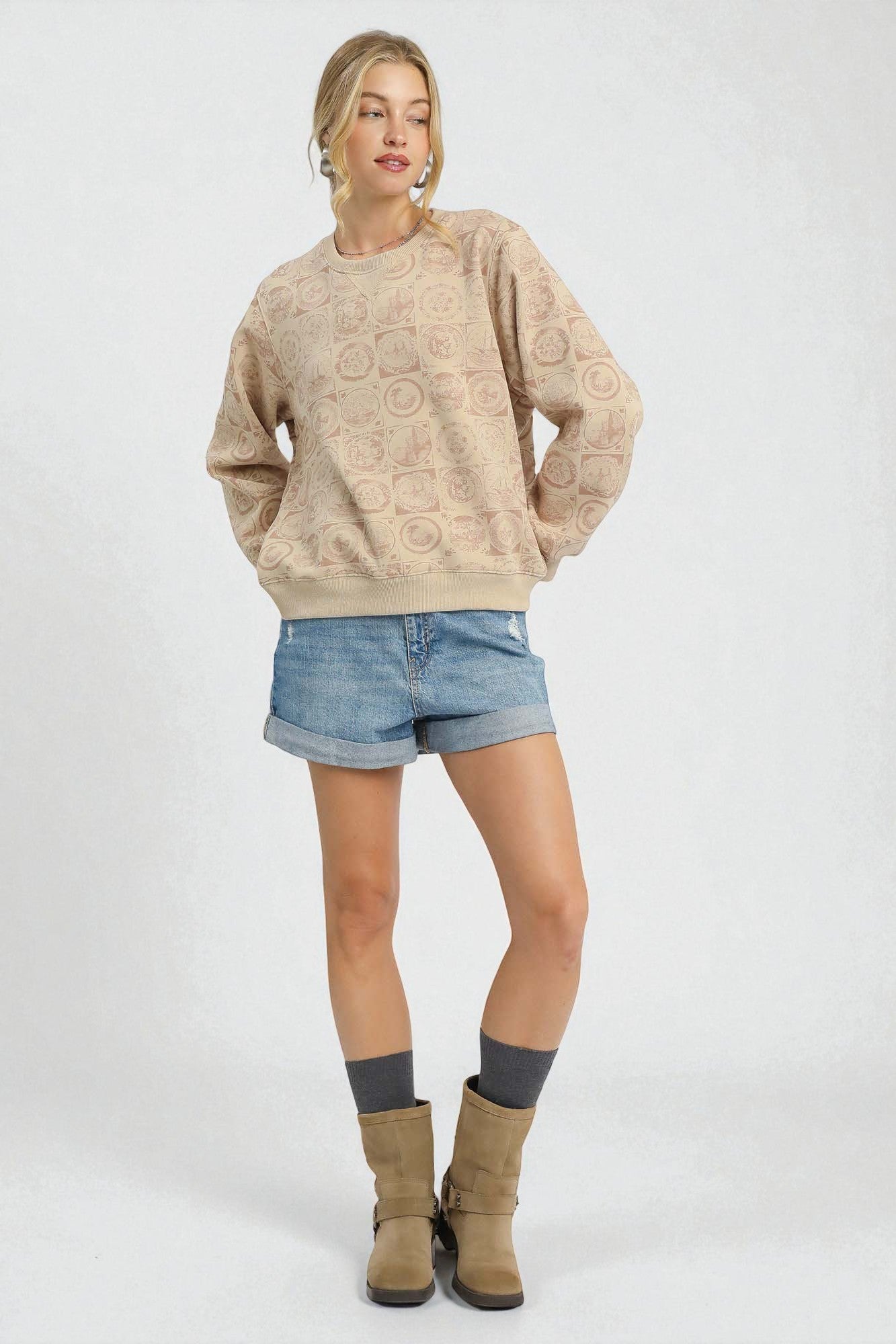 Woman wearing a beige textured sweater, denim shorts, and brown boots on a white background