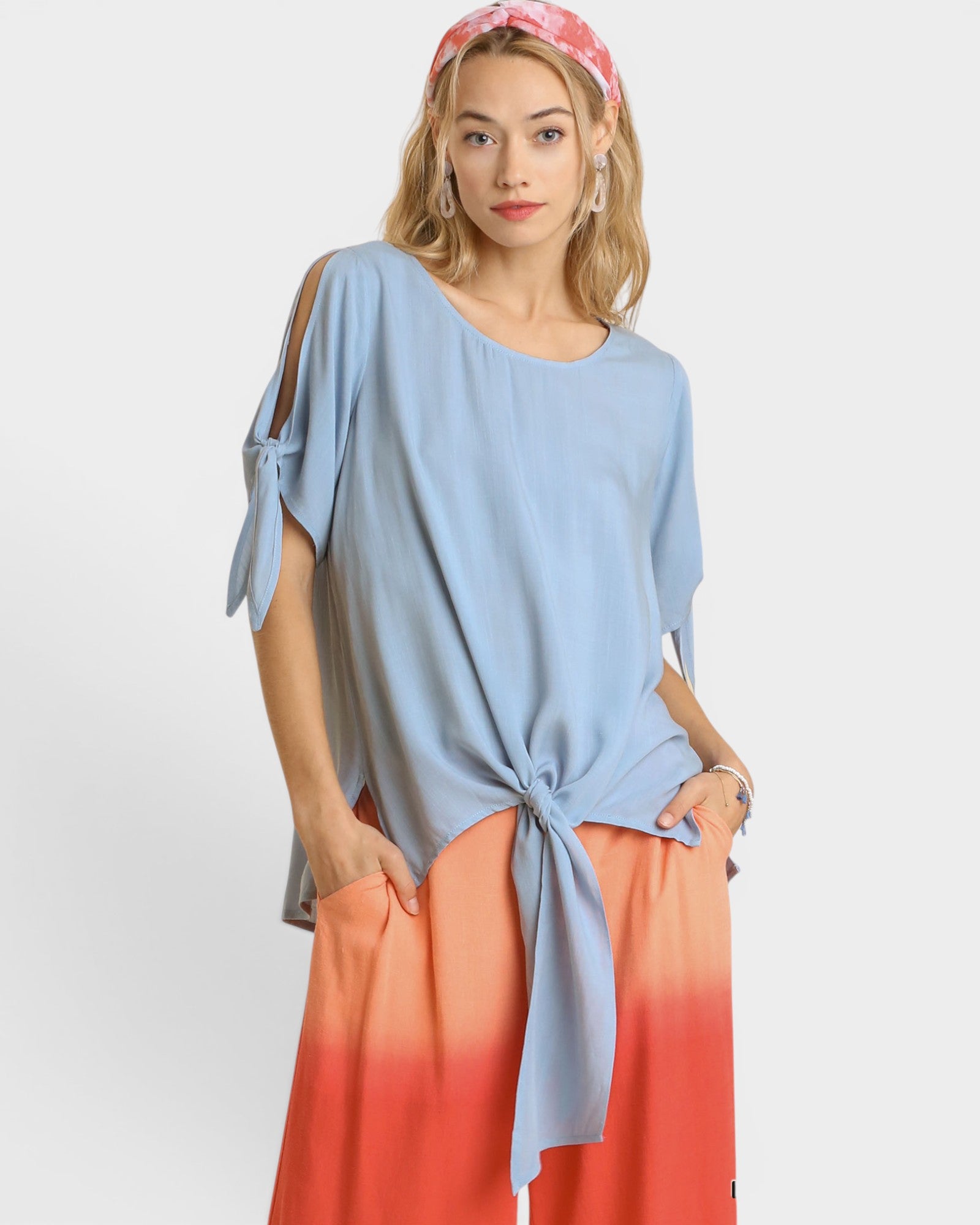 Woman wearing a light blue top with a knot detail and an ombre orange skirt on a white background