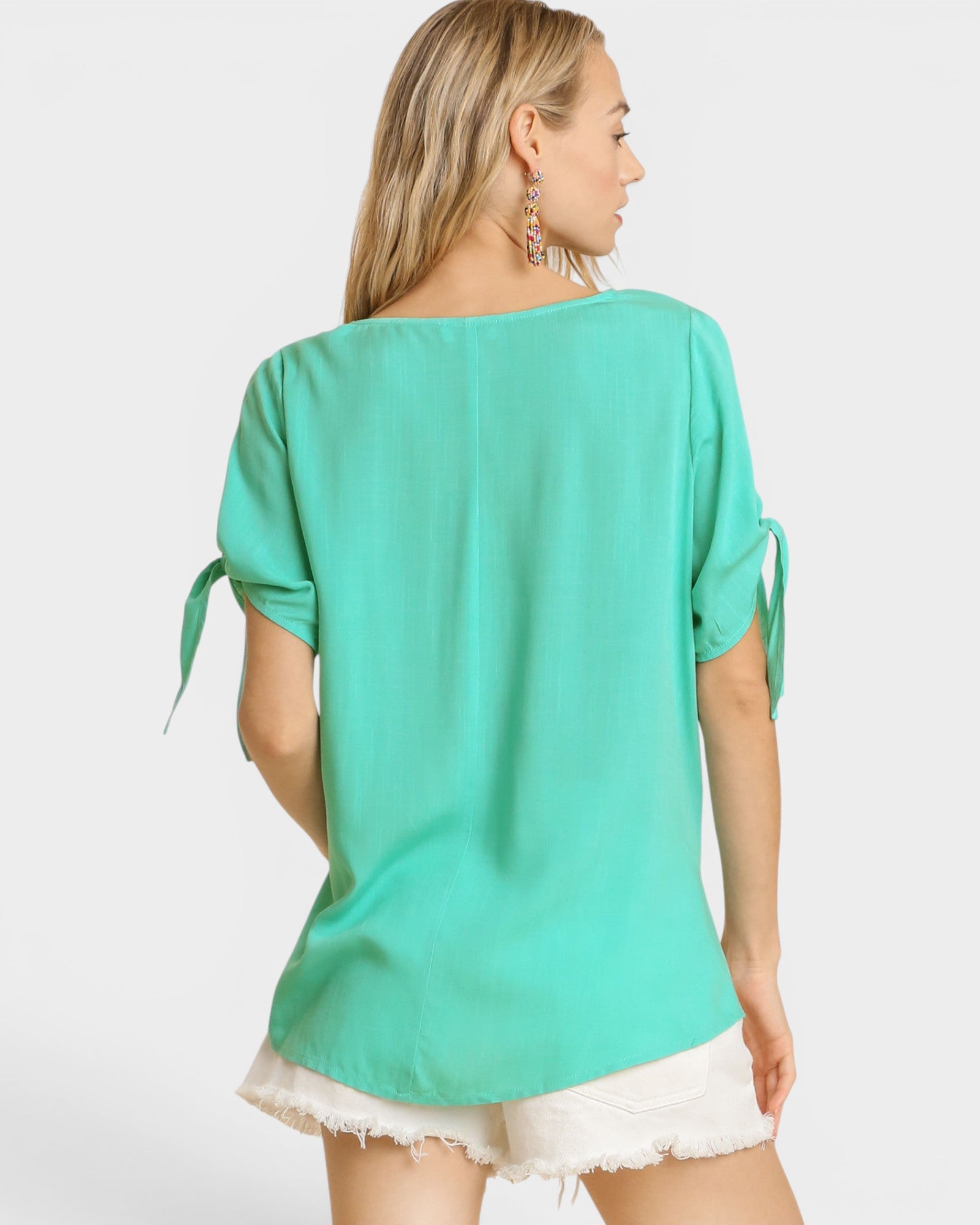 Woman wearing a teal top with tied sleeves on a white background