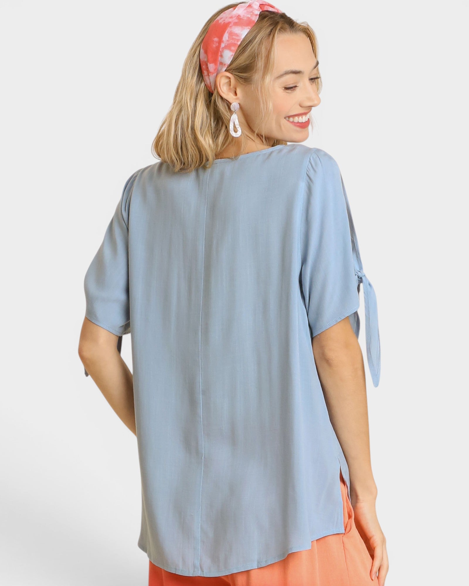Woman wearing a light blue top with tie sleeves on a white background