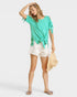 Woman wearing a green top and white shorts on a white background