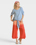 Woman wearing a blue top and red-orange pants on a white background