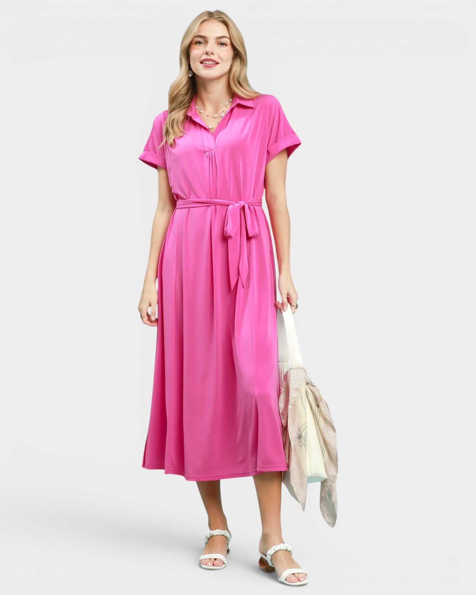 Woman wearing a pink dress holding a white bag on a plain background