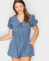 Woman wearing a blue romper with ruffled collar against a white background