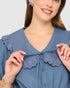 Woman wearing a blue blouse with lace details on a plain background