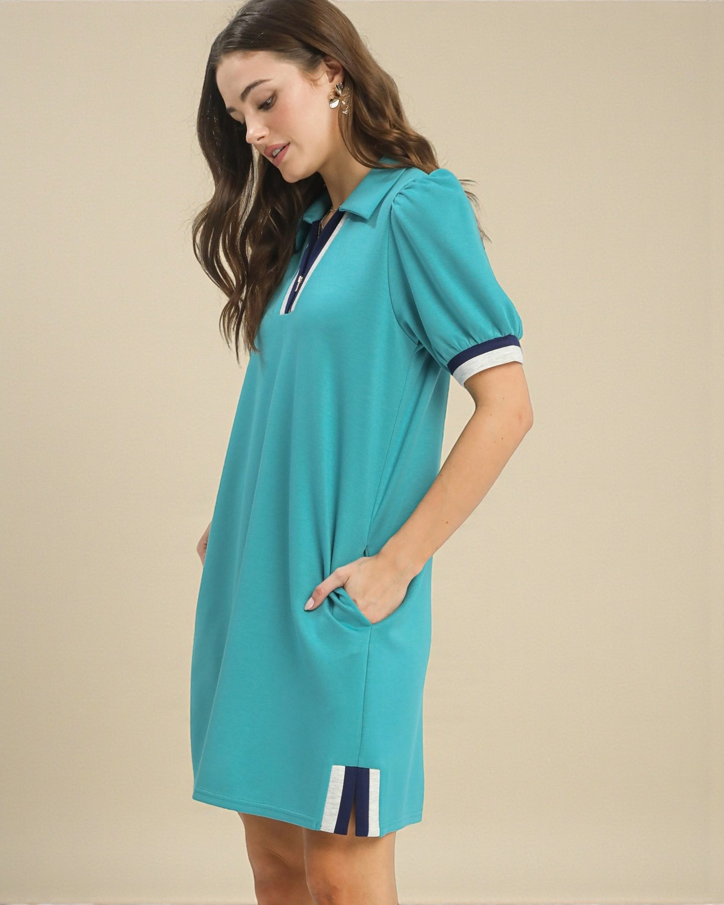 Woman wearing a turquoise dress with white trim on a beige background