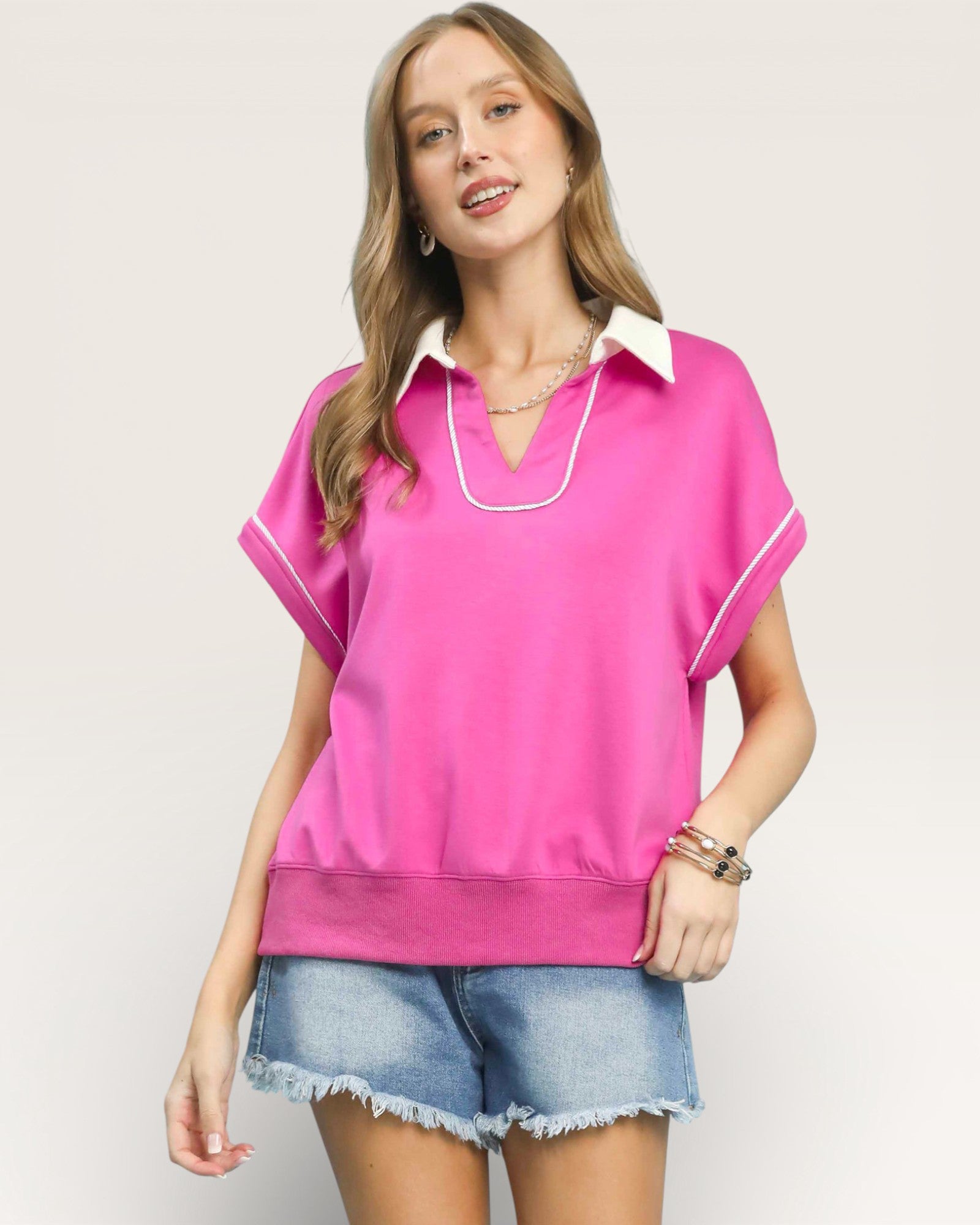 Woman wearing a pink blouse with white trim on a plain background