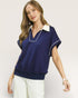 Woman wearing a navy blue blouse with white trim on a light background