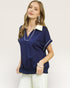 Woman wearing a navy blue blouse with white trim on a plain background